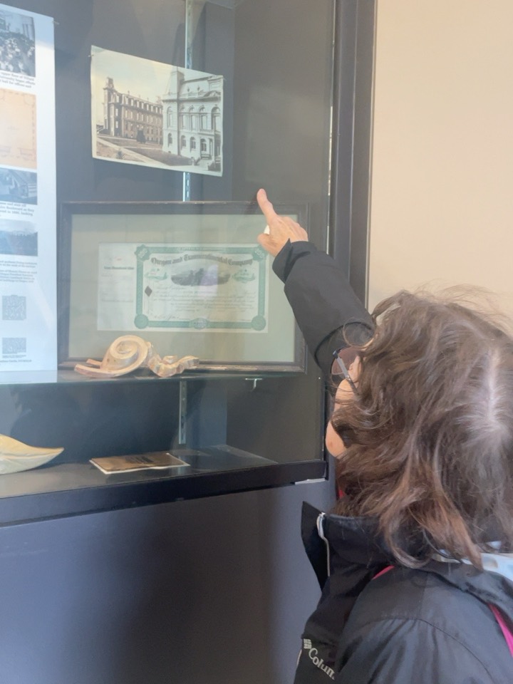 The other charter member points at an old photograph of Villard Hall in a display case inside the building.